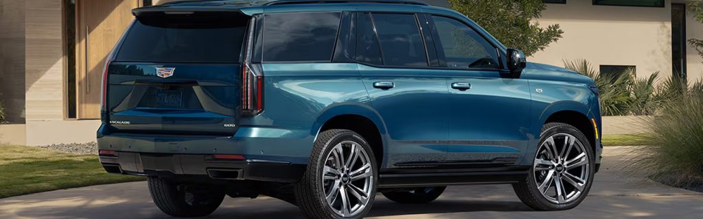 A Cadillac Escalade SUV parked in front of a modern house with a sleek blue exterior.
