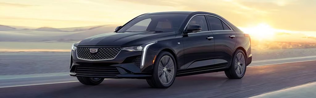 A Cadillac CT4 sedan driving on a road at sunset with a sleek black exterior.