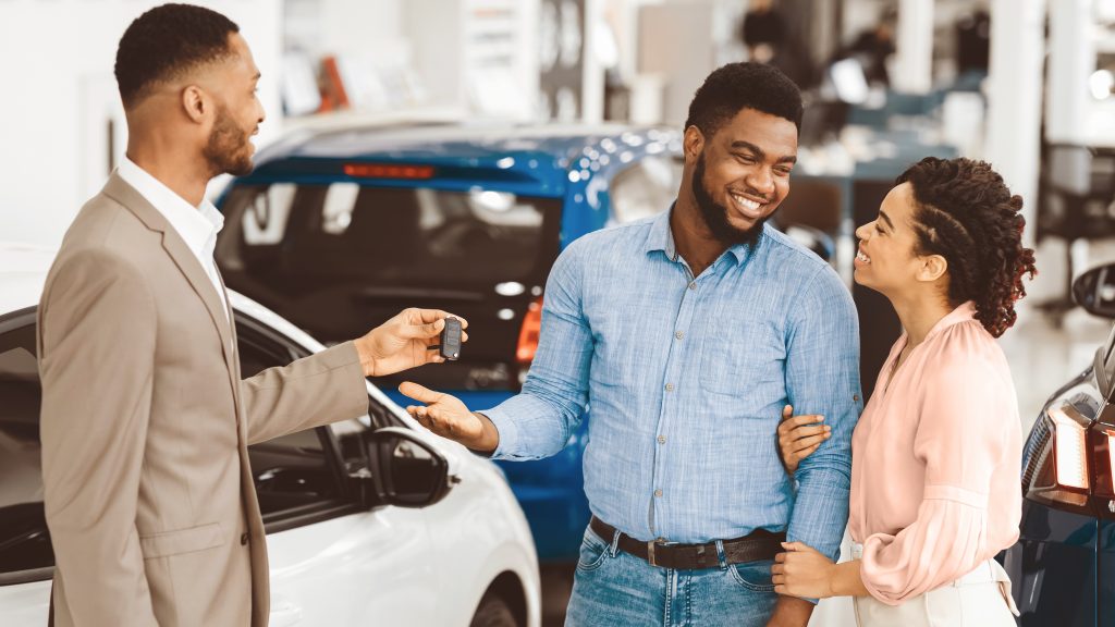 A car salesperson handing keys to a happy couple in a showroom.